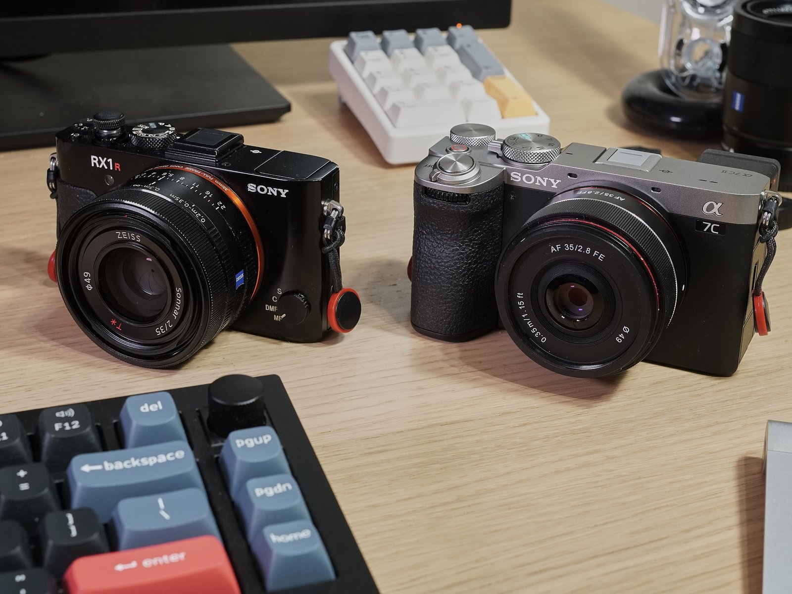 Two Sony cameras sit on a computer desk: An RX1R II and an A7C II.